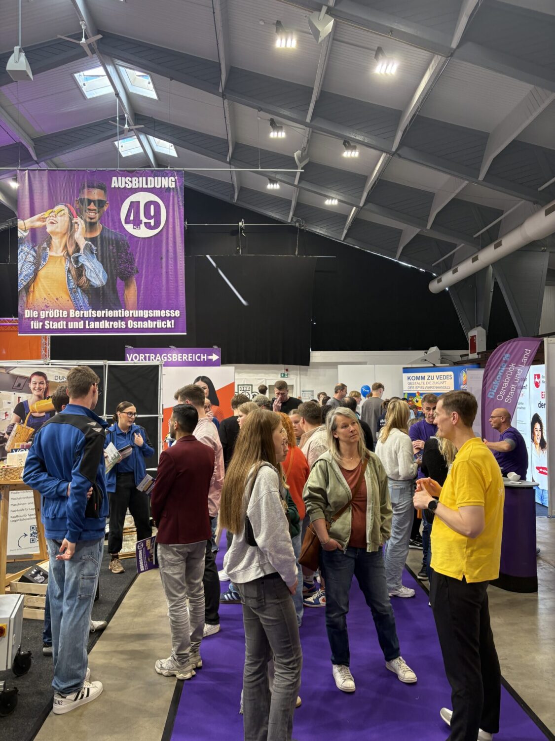 Messegeschehen: Besucher auf der Ausbildungsmesse 49. Menschen stehen an einem Stand, um sich über Berufsorientierung zu informieren.