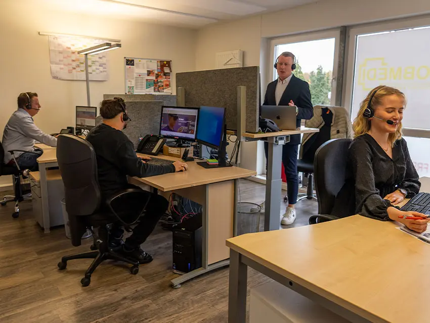 Das JF-Messekonzept-Start-Team bei der Arbeit: Mitarbeiter mit Headsets an Computern in einem hellen, modernen Büro.