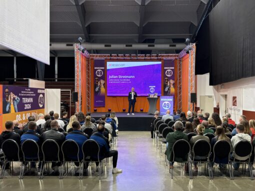 Bühne mit Vortrag über Ausbildung 49, Publikum sitzt vor der Bühne, Redner hält Vortrag. Messekonzept und Ausbildung im Fokus.